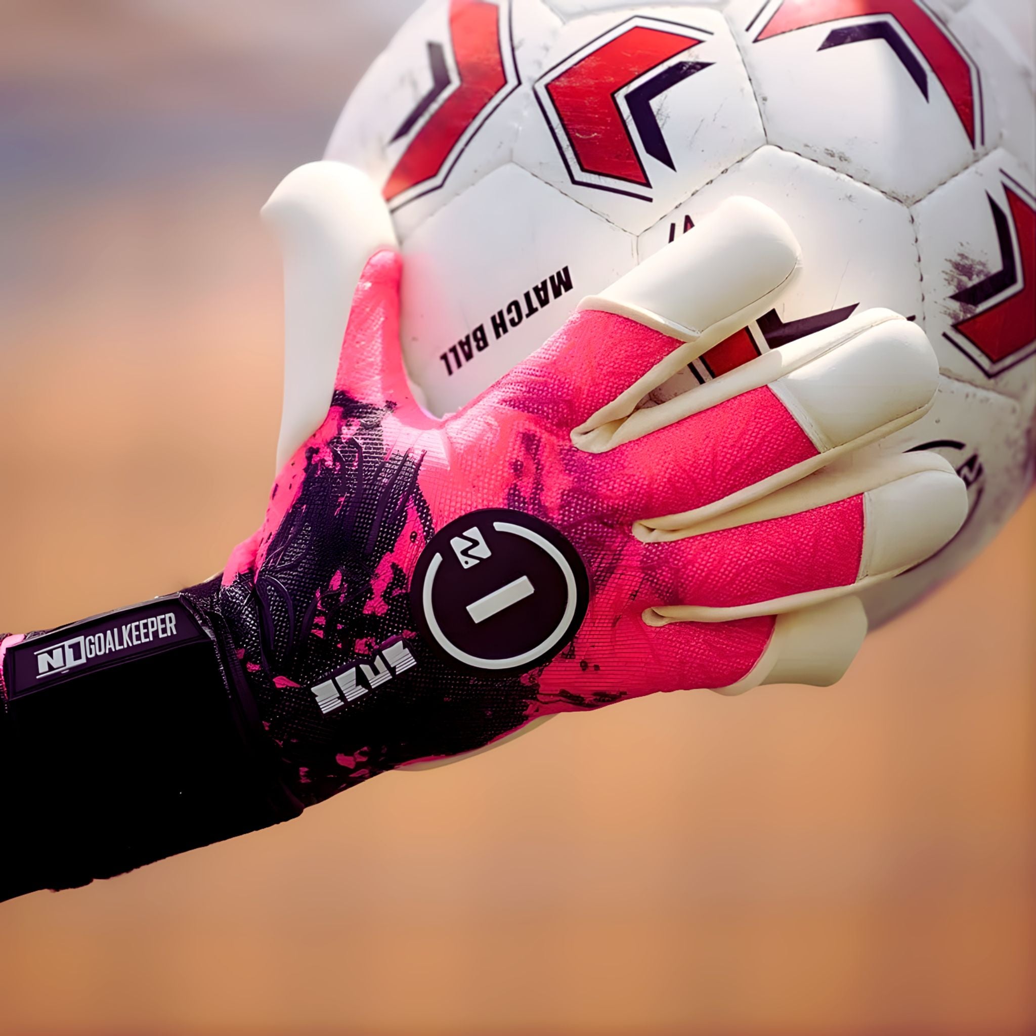 A close-up of the N1 Zeus 2.0 Storm goalkeeper glove, featuring a vibrant pink and black splatter design, securely gripping a soccer ball.